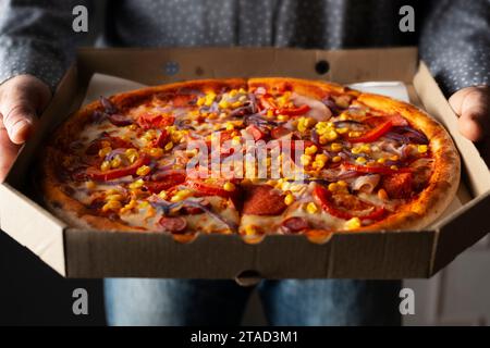 Les mains masculines caucasiennes tiennent une grande boîte en carton ouverte avec pizza pepperoni avec vue de face de maïs doux Banque D'Images