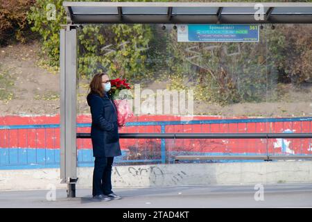 Belgrade, Serbie - 02 décembre 2020 : une femme avec un masque facial attendant les transports en commun à l'arrêt de bus tout en tenant l'usine de Poinsettia, en hiver Banque D'Images