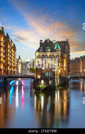 Château illuminé à douves dans le quartier historique des entrepôts de Hambourg à l'heure bleue après le coucher du soleil Banque D'Images