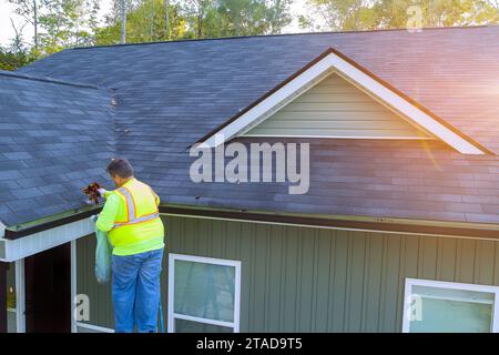 Le travailleur nettoie la saleté, les débris, les feuilles tombées du drain de gouttière de toit qui est devenu obstrué Banque D'Images