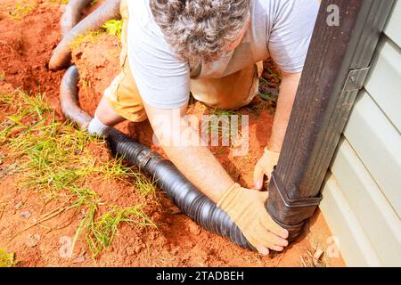 L'homme installe le tuyau de drainage de rallonge de gouttière flexible de la goulotte de descente du connecteur Banque D'Images
