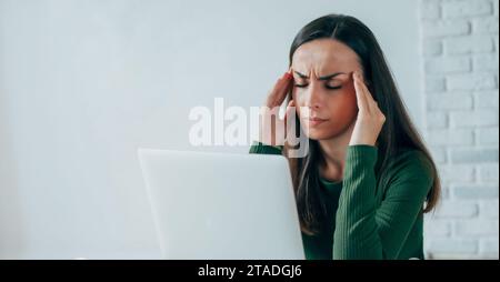 Portrait rapproché d'une jeune femme brune fatiguée, assise les yeux fermés, touchant sa tête tout en souffrant d'une migraine ou de maux de tête Banque D'Images