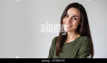 Gros plan portrait de jeune femme hispanique avec sourire toothy et bras croisés isolé sur mur gris avec espace copie. Magnifique fille en tenue décontractée looki Banque D'Images