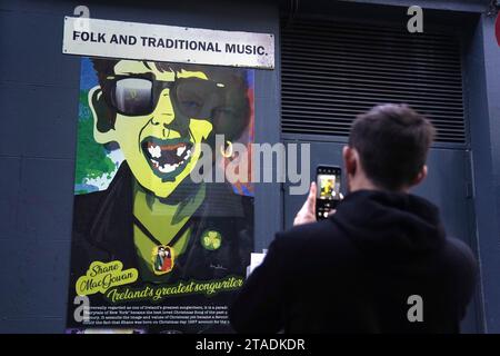 Un homme photographie une image de Shane MacGowan, chanteur principal de The Pogues, sur un bâtiment dans le quartier du Temple à Dublin. Shane MacGowan est décédé à l’âge de 65 ans, a annoncé sa femme dans un post sur Instagram. Date de la photo : jeudi 30 novembre 2023. Banque D'Images