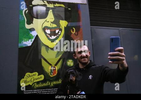 Un homme photographie une image de Shane MacGowan, chanteur principal de The Pogues, sur un bâtiment dans le quartier du Temple à Dublin. Shane MacGowan est décédé à l’âge de 65 ans, a annoncé sa femme dans un post sur Instagram. Date de la photo : jeudi 30 novembre 2023. Banque D'Images