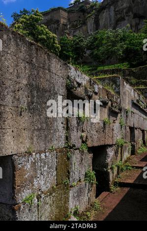 Une rangée de tombes de cube étrusque ou de chambre dans le cimetière étrusque de Crocifisso del Tufo à Orvieto, Ombrie, Italie. Les tombes étaient regroupées en blocs et disposées en rangées le long d'un réseau de chemins funéraires. Sur l'architrave ou linteau au-dessus de l'entrée de chaque tombe, inscrit en vieil italique, la langue étrusque et l'écriture, est le nom de la famille enterrée là. Banque D'Images