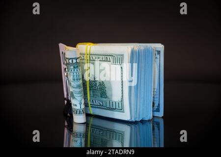 pile de billets de dollar collectés dans une bande élastique et un clip de papeterie, isolé sur un fond noir. Banque D'Images