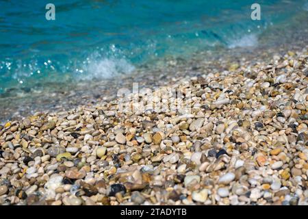 Détail en gros plan - petits cailloux ou sable rugueux sur une plage, soleil brouillé de l'après-midi illuminé mer calme en arrière-plan Banque D'Images