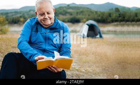 Heureux homme âgé lisant un livre en plein air pendant la journée de randonnée. Concept de vacances aventure et de voyage Banque D'Images