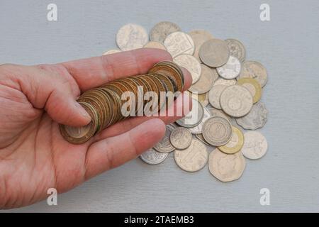 La main masculine gauche tient des pièces de monnaie bimitales sur un fond gris clair et d'autres pièces de monnaie diverses dans la paume. Banque D'Images