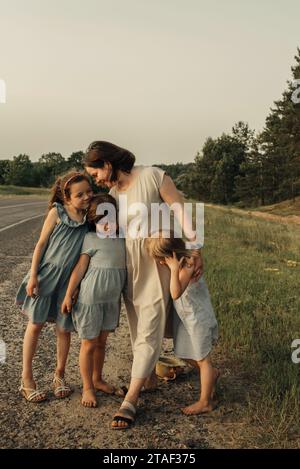 Maman embrasse ses filles sur une route rurale. L'amour de mère. Banque D'Images