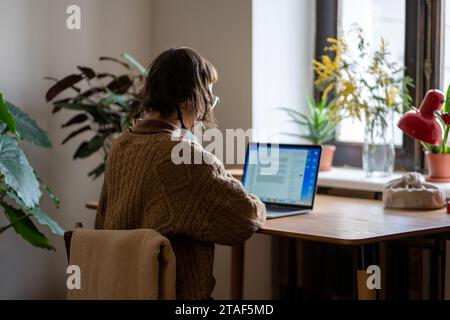 Concentré concentré femme freelance travaillant sur ordinateur portable lisant des documents assis au bureau à la maison. Banque D'Images