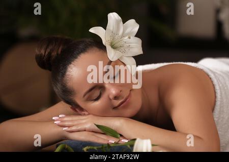 Belle jeune femme avec des fleurs se relaxant dans le salon spa sombre, closeup Banque D'Images