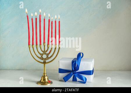 Menorah avec des bougies allumées et boîte-cadeau pour la célébration Hanukkah sur fond de couleur claire Banque D'Images