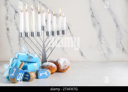 Menorah, dreidels, cadeaux et beignets pour la célébration Hanukkah sur fond clair Banque D'Images