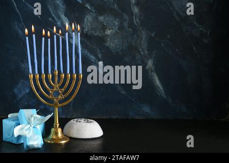 Menorah avec des bougies allumées, des cadeaux et une kippah pour la célébration Hanukkah sur fond sombre Banque D'Images