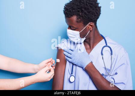 La personne caucasienne avec la seringue administre les vaccins à l'assistant médical afro-américain. Medic utilisant l'injection de vaccin sur l'infirmière masculine noire sur le bras pour la santé et l'immunité. Banque D'Images