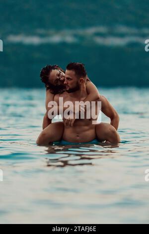 Un jeune couple romantique partageant un baiser passionné au milieu de la beauté sereine de l'océan au coucher du soleil. Banque D'Images