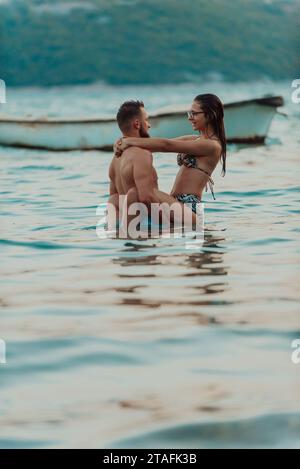 Un jeune couple romantique partageant un baiser passionné au milieu de la beauté sereine de l'océan au coucher du soleil. Banque D'Images