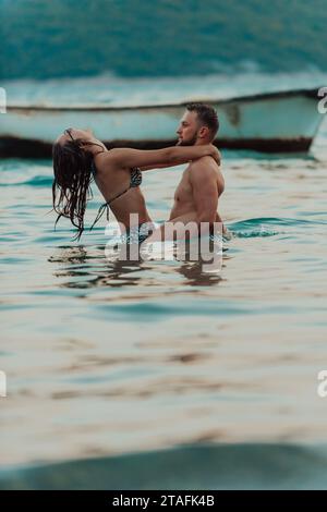 Un jeune couple romantique partageant un baiser passionné au milieu de la beauté sereine de l'océan au coucher du soleil. Banque D'Images