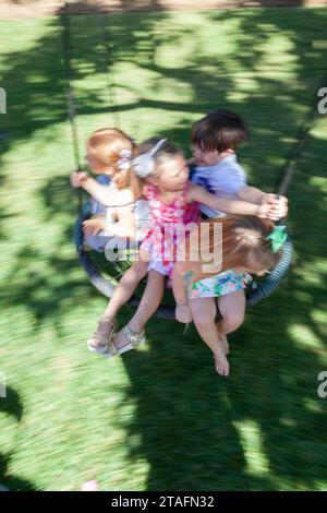Groupe d'enfants roulent ensemble sur une balançoire ronde de corde dans la cour arrière, Miami, Floride, États-Unis Banque D'Images