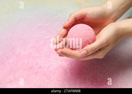 Femme tenant la bombe de bain au-dessus de l'eau avec de la mousse, gros plan. Espace pour le texte Banque D'Images