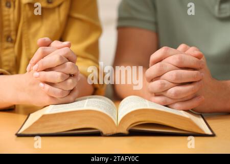 Couple de famille priant sur la Bible ensemble à table à l'intérieur, gros plan Banque D'Images