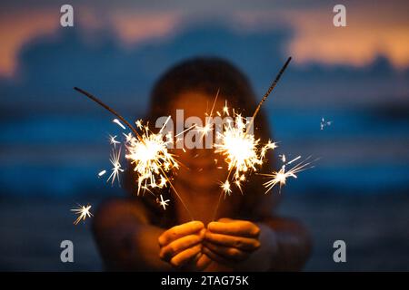 Heureuse jeune femme tenant Sparkler célébrant la veille du nouvel an sur la plage Banque D'Images