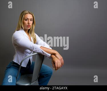 Brawny Body Builder Belle jeune femme expression réfléchie assise face à la caméra gris fond gris Copy Space Banque D'Images