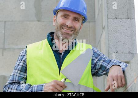 heureux constructeur professionnel dans le casque est plâtrant le mur Banque D'Images