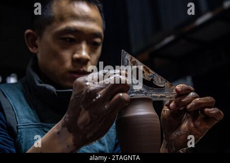 (231201) -- CHONGQING, 1 déc. 2023 (Xinhua) -- Guan Yongshuang réalise une œuvre d'art en poterie dans son atelier du district de Rongchang à Chongqing, dans le sud-ouest de la Chine, le 14 novembre 2023. Liang Xiancai, 73 ans, est un héritier de l'artisanat de poterie de Rongchang, un patrimoine culturel immatériel en Chine. Malgré la tendance à la mécanisation, à l'automatisation et à la production de poterie à grande échelle, il maintient fermement la tradition de la poterie manuelle. Guan Yongshuang, 32 ans, est diplômé de l'Institut des Beaux-Arts du Sichuan avec une majeure en art potier Il étudie la culture de la poterie depuis près de dix ans. Guan Banque D'Images