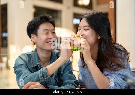 Joyeux et charmant jeune couple asiatique aime manger un délicieux hamburger sur un rendez-vous de week-end dans un restaurant dans la ville ensemble. rencontres, relation, happ Banque D'Images