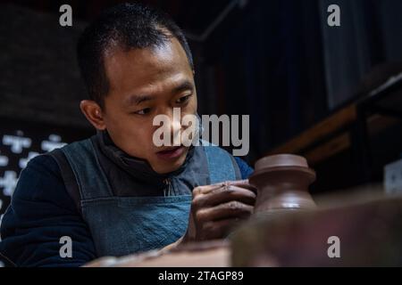 (231201) -- CHONGQING, 1 déc. 2023 (Xinhua) -- Guan Yongshuang réalise une œuvre d'art en poterie dans son atelier du district de Rongchang à Chongqing, dans le sud-ouest de la Chine, le 14 novembre 2023. Liang Xiancai, 73 ans, est un héritier de l'artisanat de poterie de Rongchang, un patrimoine culturel immatériel en Chine. Malgré la tendance à la mécanisation, à l'automatisation et à la production de poterie à grande échelle, il maintient fermement la tradition de la poterie manuelle. Guan Yongshuang, 32 ans, est diplômé de l'Institut des Beaux-Arts du Sichuan avec une majeure en art potier Il étudie la culture de la poterie depuis près de dix ans. Guan Banque D'Images