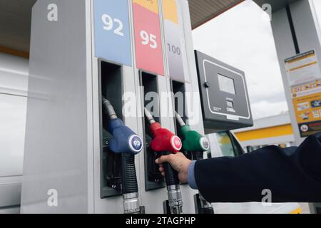 homme d'affaires en costume gère sa voiture avec de l'essence dans une station-service. Gros plan sur les pistolets à carburant à main et rouge. Banque D'Images