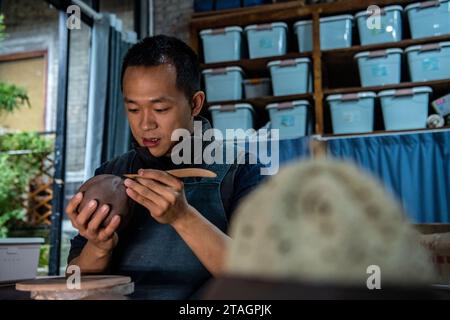 (231201) -- CHONGQING, 1 déc. 2023 (Xinhua) -- Guan Yongshuang réalise une œuvre d'art en poterie dans son atelier du district de Rongchang à Chongqing, dans le sud-ouest de la Chine, le 14 novembre 2023. Liang Xiancai, 73 ans, est un héritier de l'artisanat de poterie de Rongchang, un patrimoine culturel immatériel en Chine. Malgré la tendance à la mécanisation, à l'automatisation et à la production de poterie à grande échelle, il maintient fermement la tradition de la poterie manuelle. Guan Yongshuang, 32 ans, est diplômé de l'Institut des Beaux-Arts du Sichuan avec une majeure en art potier Il étudie la culture de la poterie depuis près de dix ans. Guan Banque D'Images