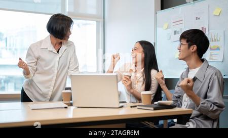 Un patron se sent satisfait du résultat d'un projet et fait un compliment à ses collègues. Deux jeunes employés de bureau célèbrent la réussite de leur projet Banque D'Images