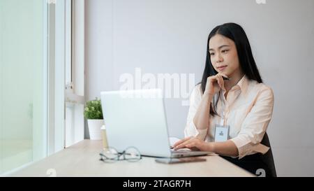 Une femme d'affaires asiatique spécialisée et professionnelle travaille sur son ordinateur portable au bureau, pensant et planifiant un nouveau projet. Banque D'Images