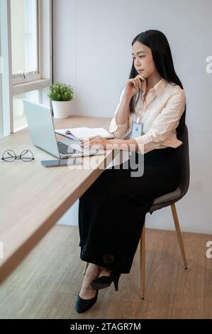 Une femme d'affaires asiatique spécialisée et professionnelle travaille sur son ordinateur portable au bureau, pensant et planifiant un nouveau projet. Banque D'Images
