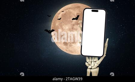 Skeleton Hand tient une maquette de smartphone avec la pleine lune et les chauves-souris, une idée créative. App et téléphone, concept. Publicité pour Halloween. Copier l'espace pour d Banque D'Images
