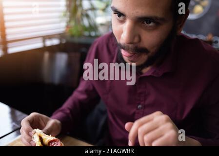 Concept de pizza Time. Employé de bureau africain masculin positif ou entrpreneur en costume mangeant un gros morceau de pizza Banque D'Images