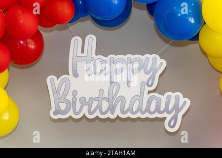 Signe papier joyeux anniversaire. Lettres argentées. Police. Entouré de ballons colorés. Rouge, jaune et bleu. Banque D'Images