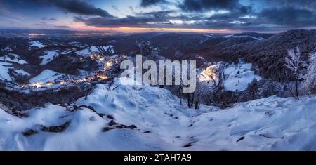 Panorama de nuit Carpates hiver village de montagne dans la lumière avec des maisons en bois sur une colline couverte de neige fraîche. Banque D'Images