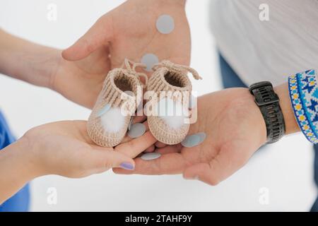 Futurs parents tenant dans leurs mains des chaussons pour nouveau-né. Famille attendant la naissance d'un bébé. Chemise ukrainienne brodée. Gros plan. Banque D'Images