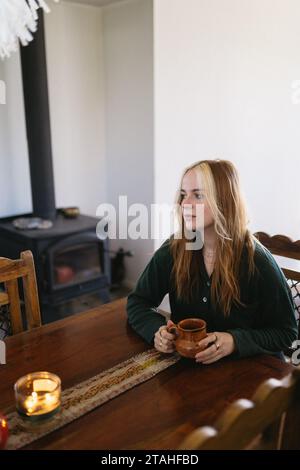 Femme assise à la table de cuisine avec tasse à café dans la cabine confortable Banque D'Images