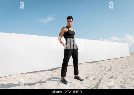 Musclé jeune cubain en tenue noire posant les mains dans les poches à Miami, South Beach Banque D'Images