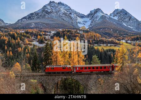 Ftan, Suisse - novembre 06. 2022 : le train rouge du chemin de fer rhétique passe avec le château de Tarasp en arrière-plan, Canton des Grisons Banque D'Images