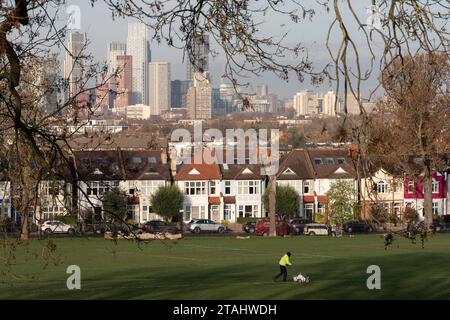 Devant les maisons de Lambeth et la ligne d'horizon de Nine Elms au loin, un employé marque les lignes blanches sur un terrain de football à Ruskin Park, un espace vert public utilisé pour les matchs de ligue locale, de jeunesse et amateur, le 29 novembre 2023, à Londres, en Angleterre. Banque D'Images