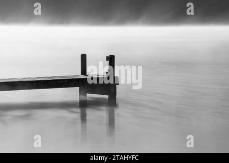 Une jetée en bois faisant saillie sur un lac dans une atmosphère brumeuse, en niveaux de gris Banque D'Images