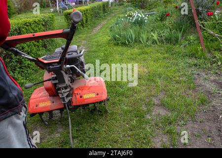 Cultivateur à moteur avec une roue avant relevée et un sillon inséré dans le sol pendant le labourage du champ avant de semer des semences et de planter des semences Banque D'Images