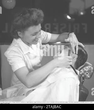 Se raser dans les années 1940 Une jeune femme rase un homme au salon de coiffure. Elle utilise un rasoir droit et est photographiée ici tout en rasant soigneusement près de l'oreille de l'homme. 1945. Photo Kristoffersson réf. N97-6 Banque D'Images